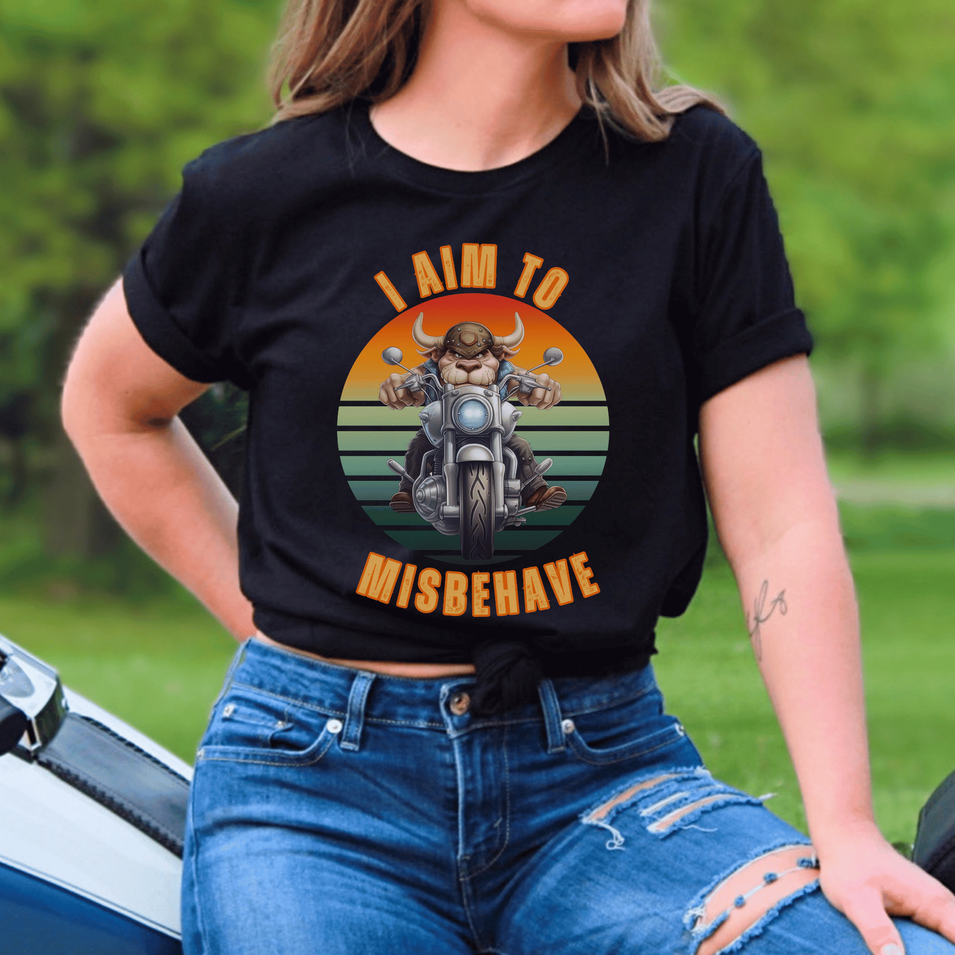 Funny tee with a bull that is riding a motorcycle with a vintage scene and text that says I aim to misbehave ptinted on a round neck t-shirt.