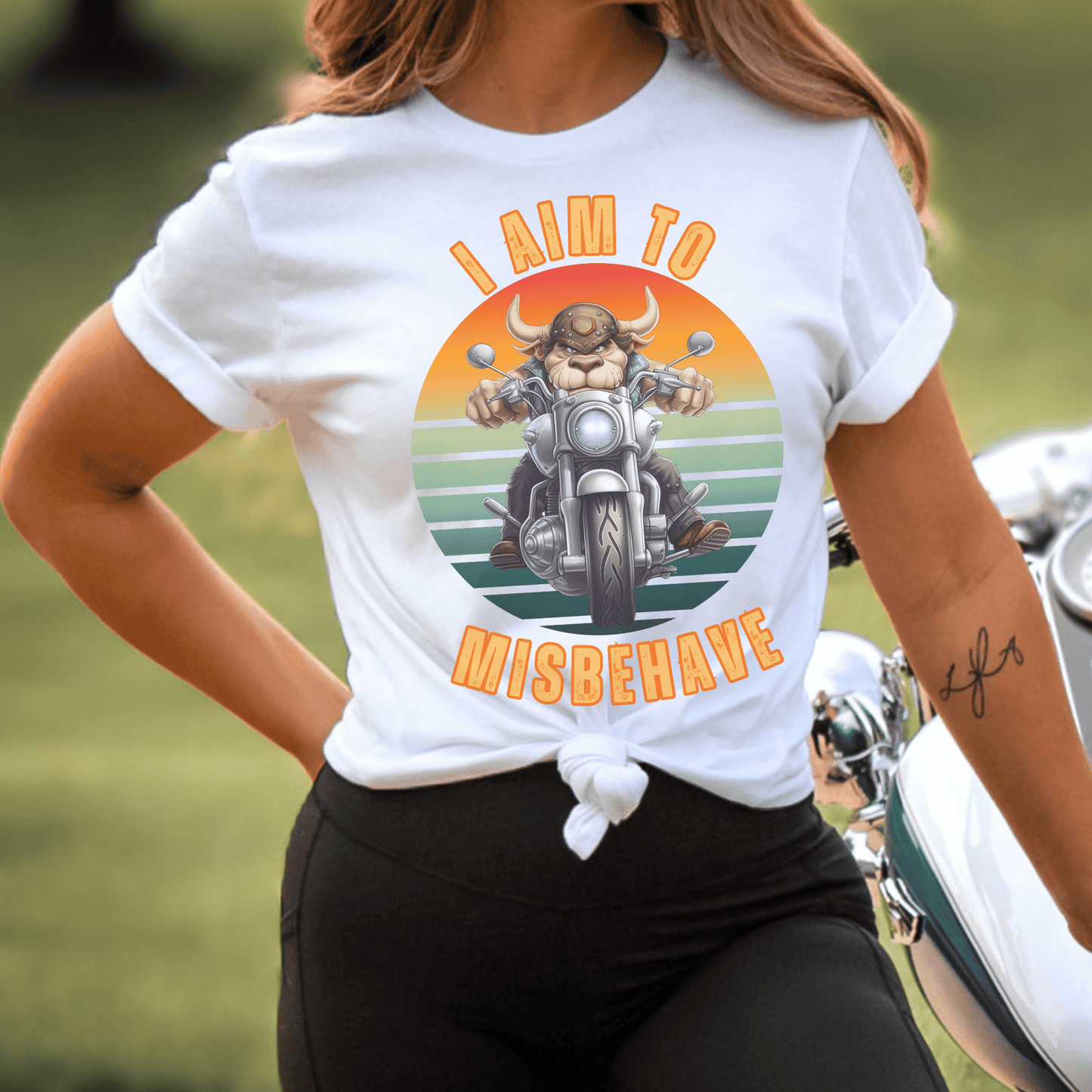 Funny tee with a bull that is riding a motorcycle with a vintage scene and text that says I aim to misbehave ptinted on a round neck t-shirt.