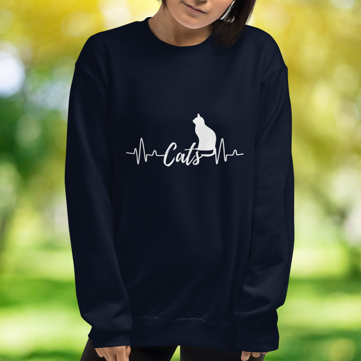 Sitting cat silhouette with a heartbeat with the word Cats in the middle of the heartbeat. The design is all white on a Navy sweatshirt.