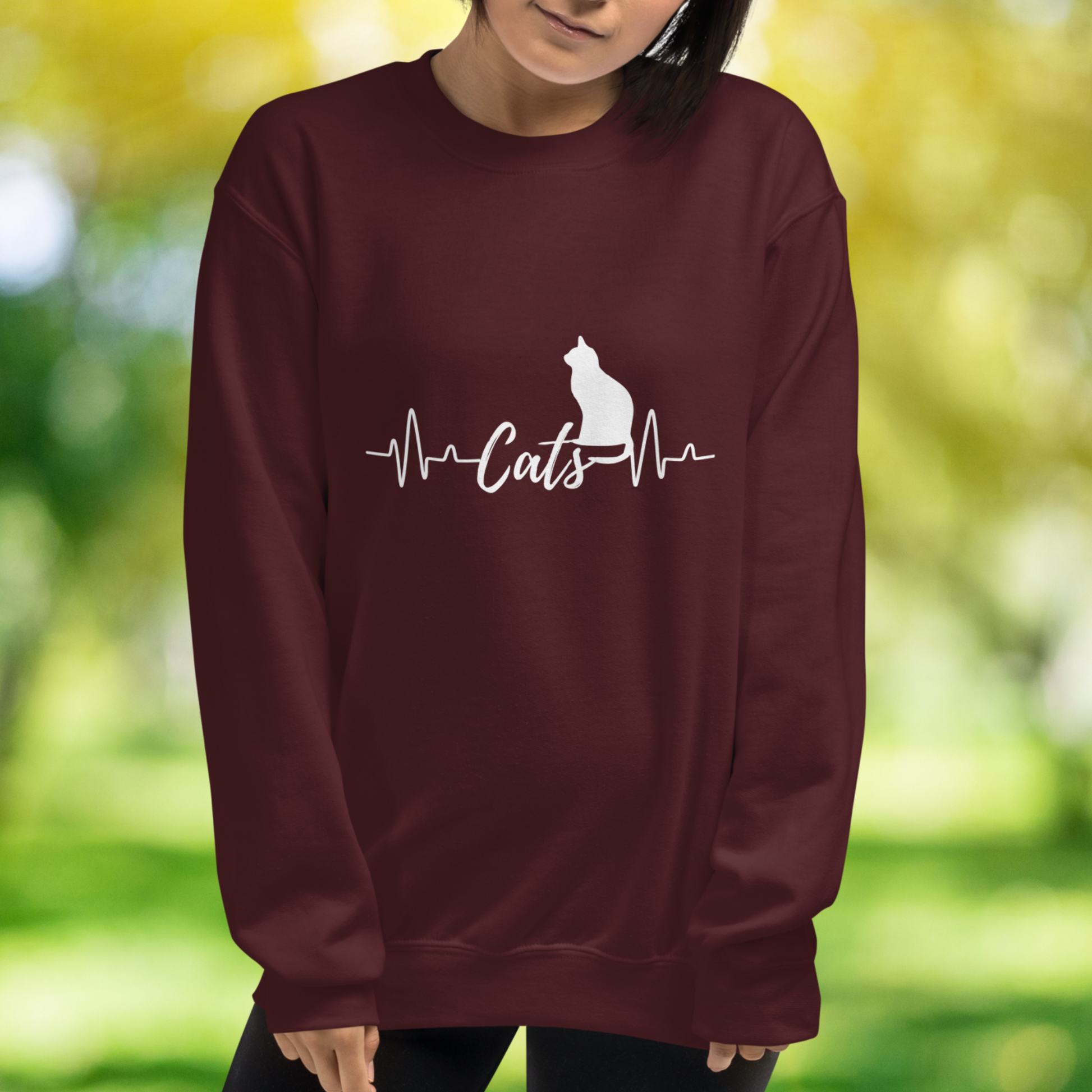 Sitting cat silhouette with a heartbeat with the word Cats in the middle of the heartbeat. The design is all white on a Maroon sweatshirt.