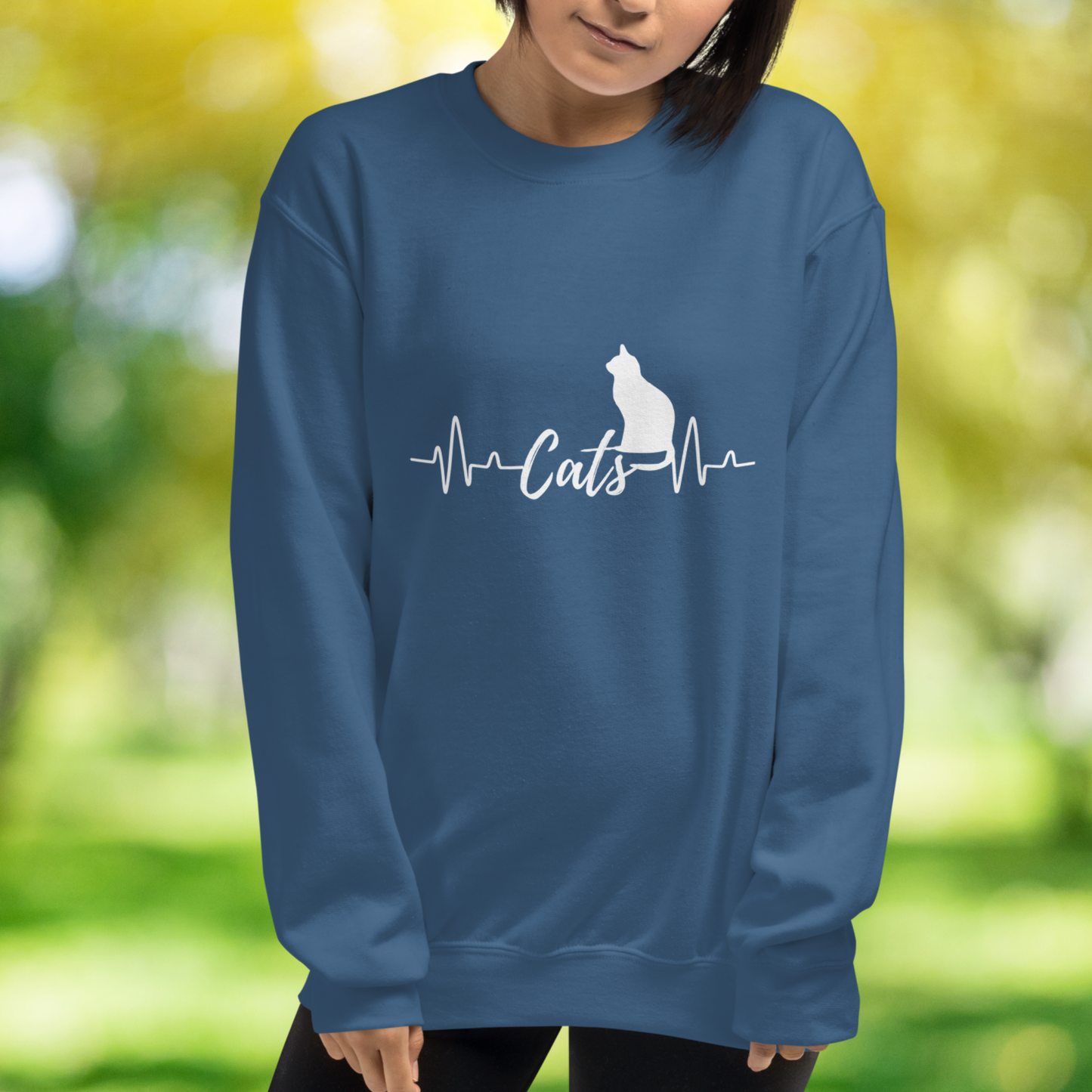 Sitting cat silhouette with a heartbeat with the word Cats in the middle of the heartbeat. The design is all white on a Indigo blue sweatshirt.