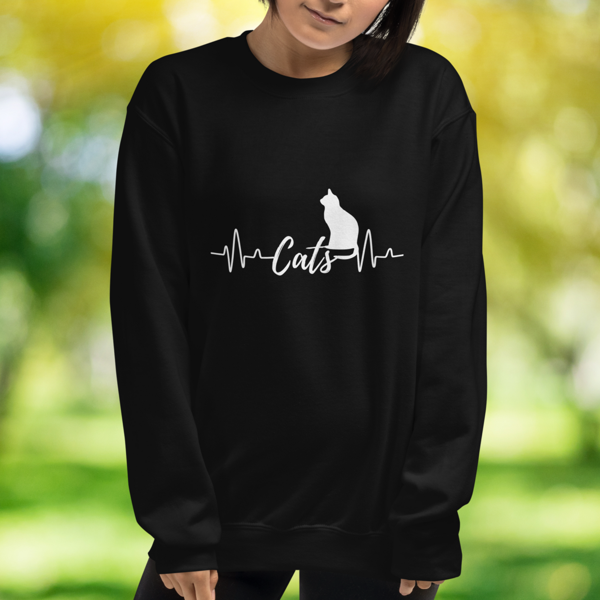 Sitting cat silhouette with a heartbeat with the word Cats in the middle of the heartbeat. The design is all white on a Black sweatshirt.